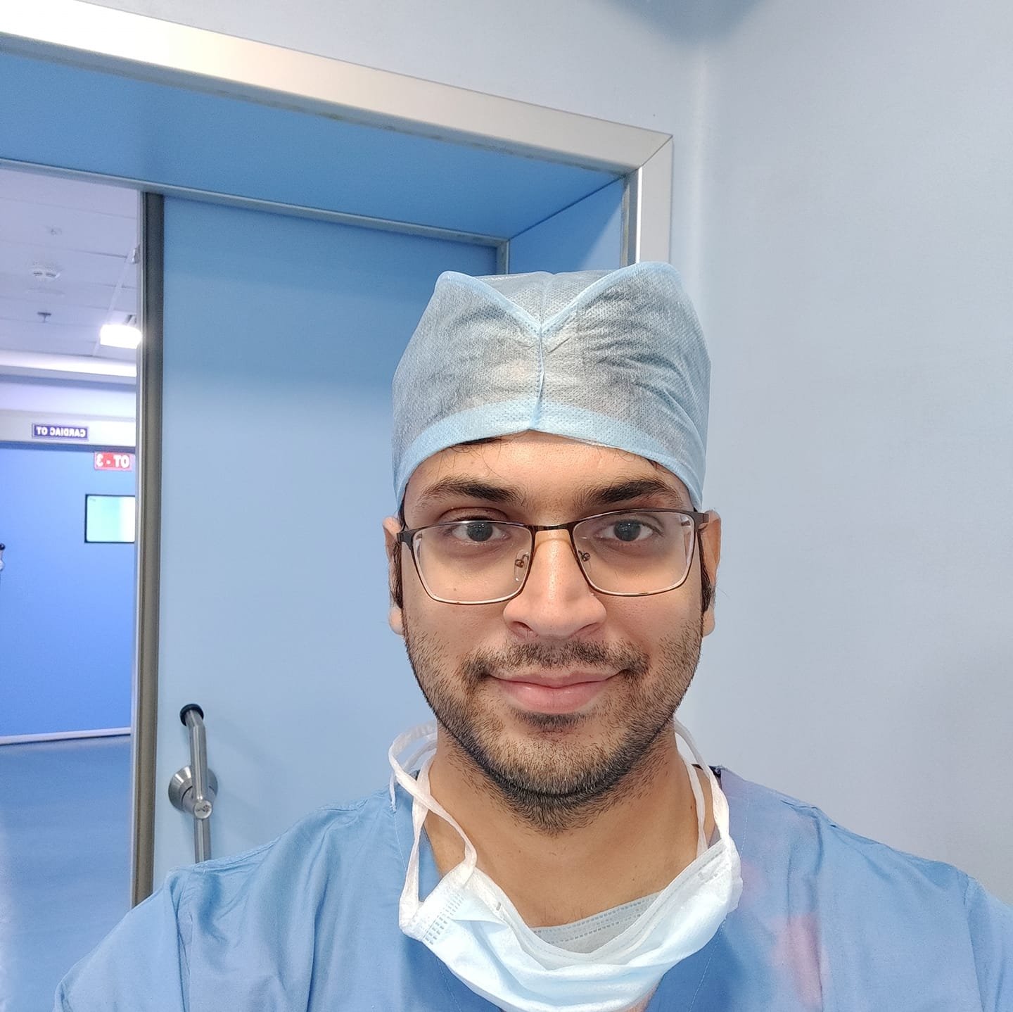 Photo of Dr. Hozefa Lokhandwala, a surgical oncologist, in surgical scrubs and cap standing in a hospital corridor.